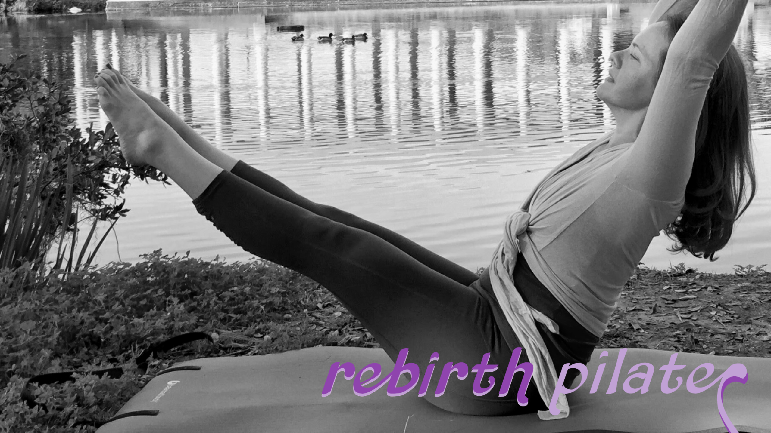 A black and white image of a  white woman with long hair wearing a wrap top and gray cropped yoga pants performing a pilates teaser in the park. In the background is a body of water, and an open air columned structure. At the bottom right of the image is the logo Rebirth Pilates in purple and lavender. 